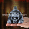 A hand holds a dark gray stone sculpture of an Aztec death whistle skull with intricate facial details.