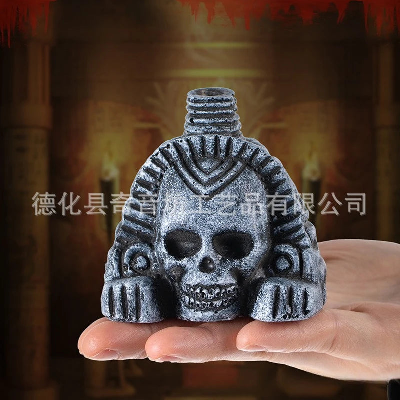 A hand holds a dark gray stone sculpture of an Aztec death whistle skull with intricate facial details.