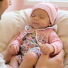 A close-up of a baby sleeping peacefully in a pink knitted hat, being held by an adult.