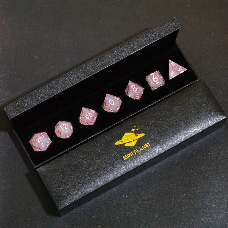 A set of pink resin polyhedral dice displayed in a black box with a gold planet logo.