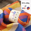A close-up of three balls of gradient acrylic yarn in orange, purple, and blue stacked on a knitted fabric background.
