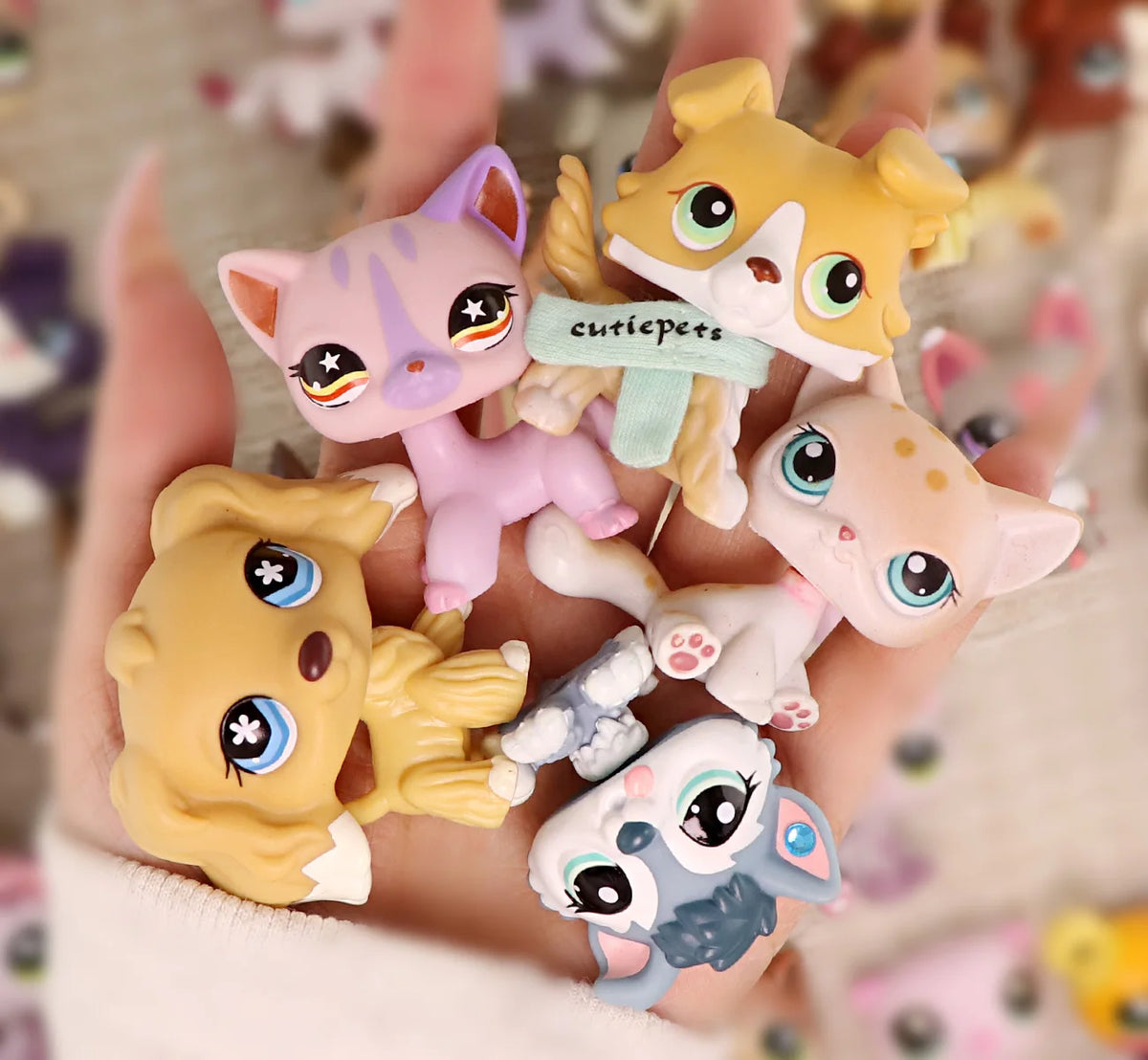 A hand holds a set of miniature pet animal figures including a pink cat, a yellow fox, and several other small animals.