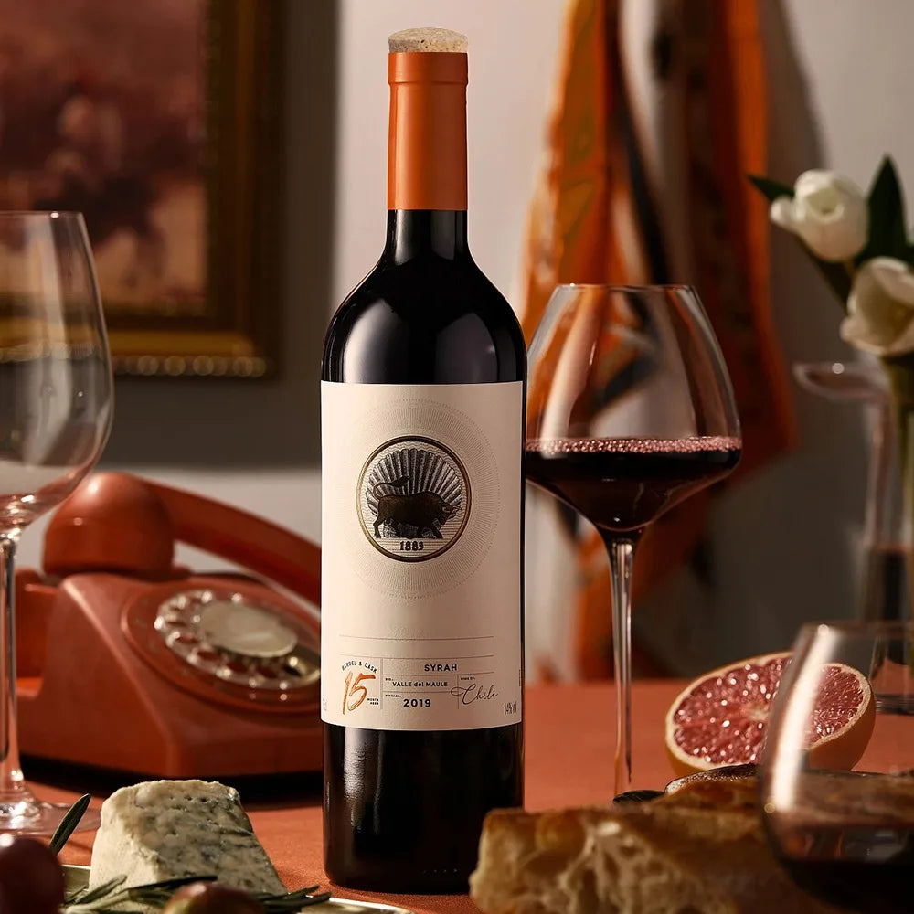 A bottle of red wine with a natural wood tapered bottle and test tube stopper is displayed on a wooden table.