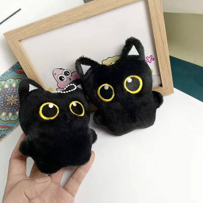 A hand holds a black cat plush cushion with yellow eyes and white trim, displayed in front of a wooden frame.