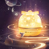 A glowing yellow spherical night light projector emitting swirling galaxy patterns and musical notes against a dark starry ba