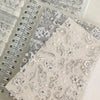 A close-up of a sticker book with 32 sheets featuring delicate gray and white floral and decorative designs for journaling.