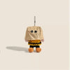 A tan plush charm resembling a cartoon character with black eyes and yellow accents, hanging from a chain.