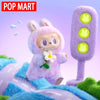 A fluffy purple Labubu plush doll with white flower accessory standing in a soft green and blue landscape.