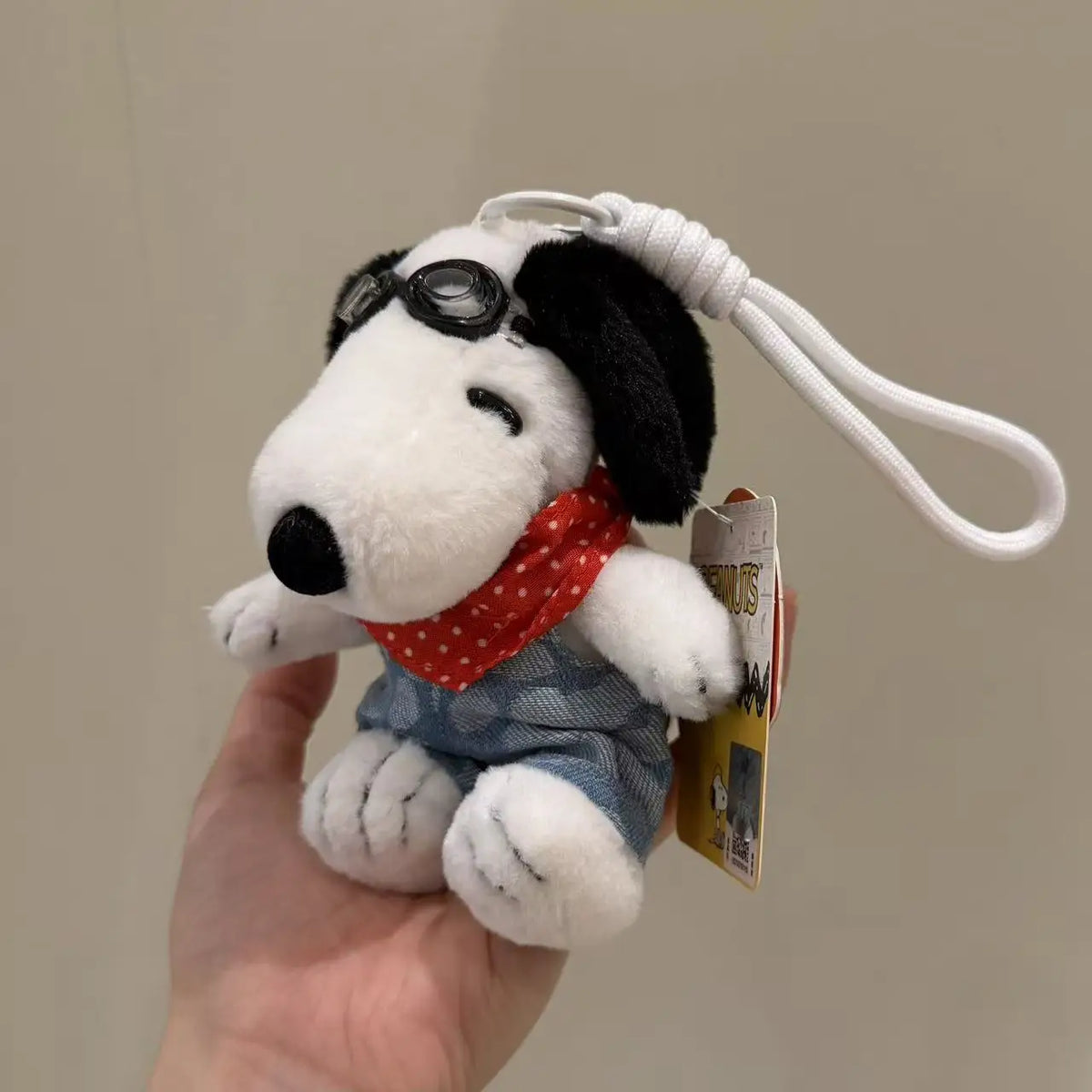 A white Snoopy plush toy with black ears and sunglasses is being held, attached to a white cord.