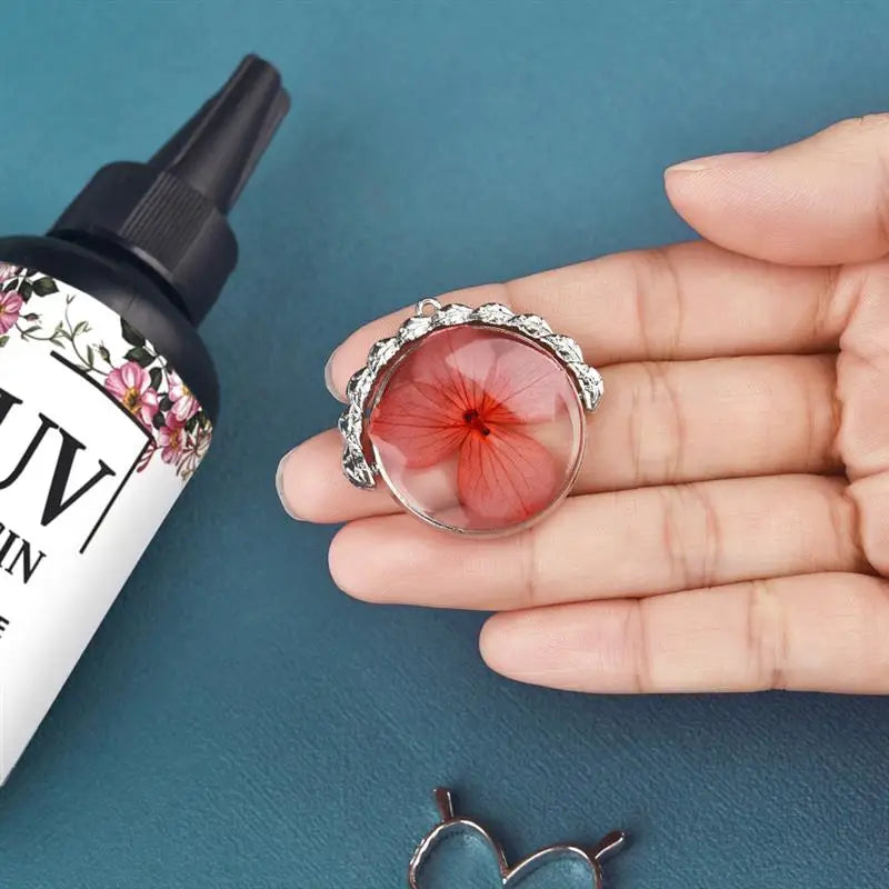 A hand holds a small, clear UV resin glue for jewelry making with a floral-edged cap.