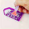 A hand is using a tool to apply white beads onto a purple diamond painting canvas.
