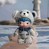 A small, gray bear-shaped plush doll with blue hair is sitting on a light brown surface.