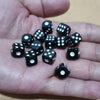 A hand holds a pile of ten black and white six-sided dice on a light surface.