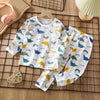 A white cotton pajama set for children featuring a repeating pattern of birds and rainbows on a wooden surface.