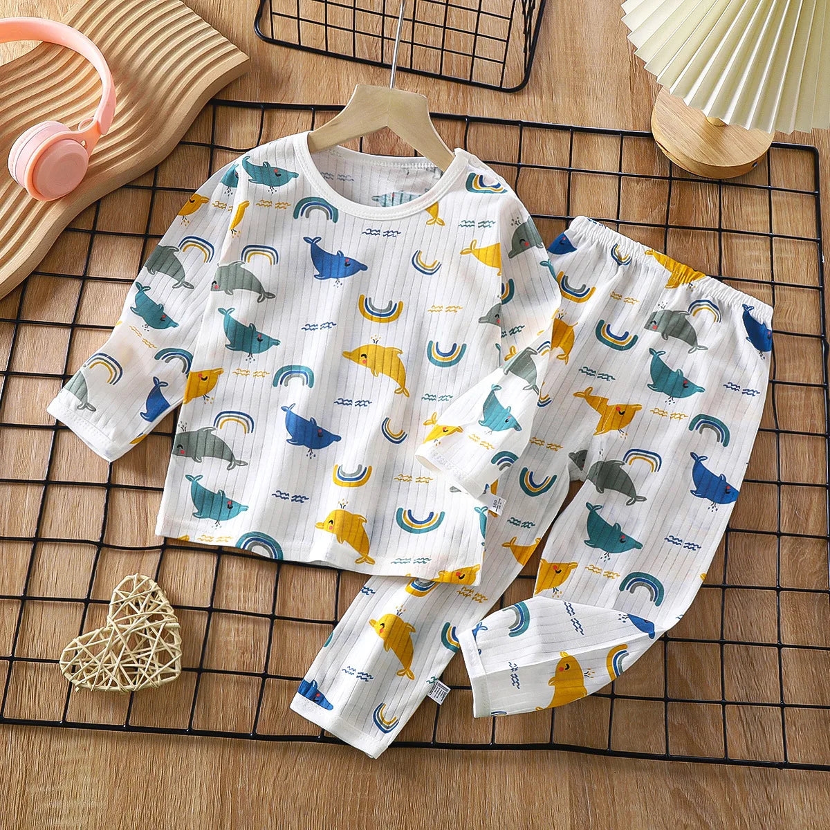 A white cotton pajama set for children featuring a repeating pattern of birds and rainbows on a wooden surface.