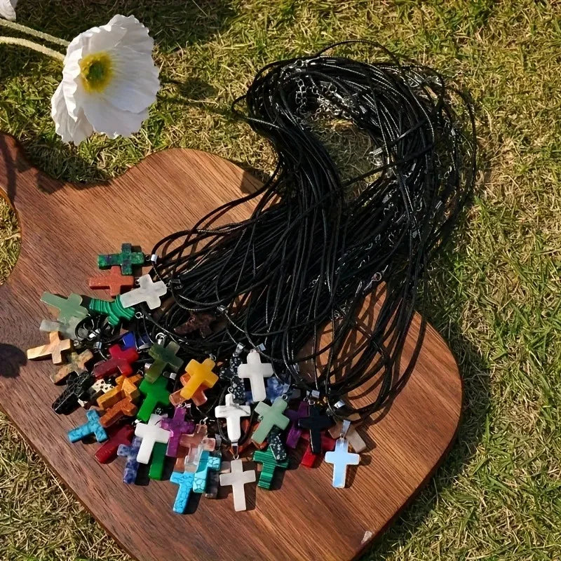 A collection of natural stone cross pendants and black wire, laid out on a wooden surface in grass.