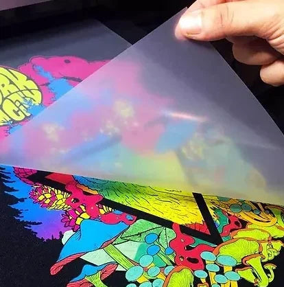 A hand holds a transparent iron-on patch featuring colorful graffiti art on a dark background.