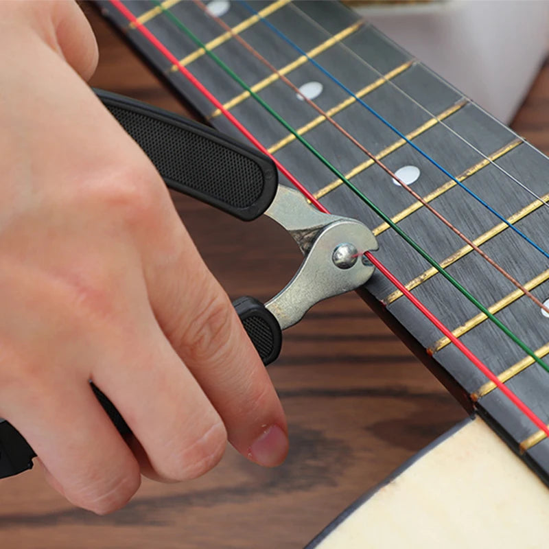 A hand is using a metal tool to wind or cut guitar strings on a fretboard.