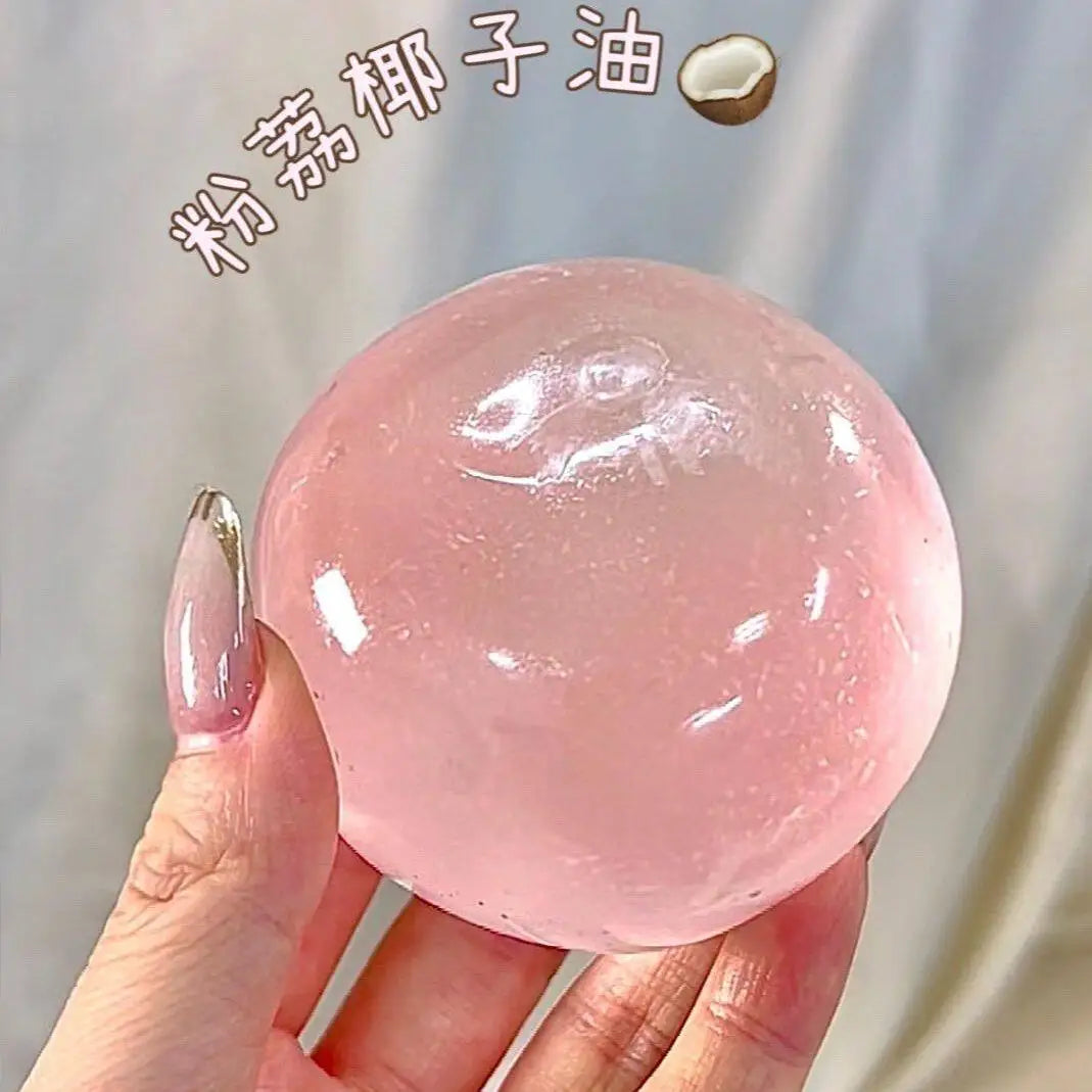 A hand holds a large, pink, translucent squeeze ball made of coconut oil for stress relief.