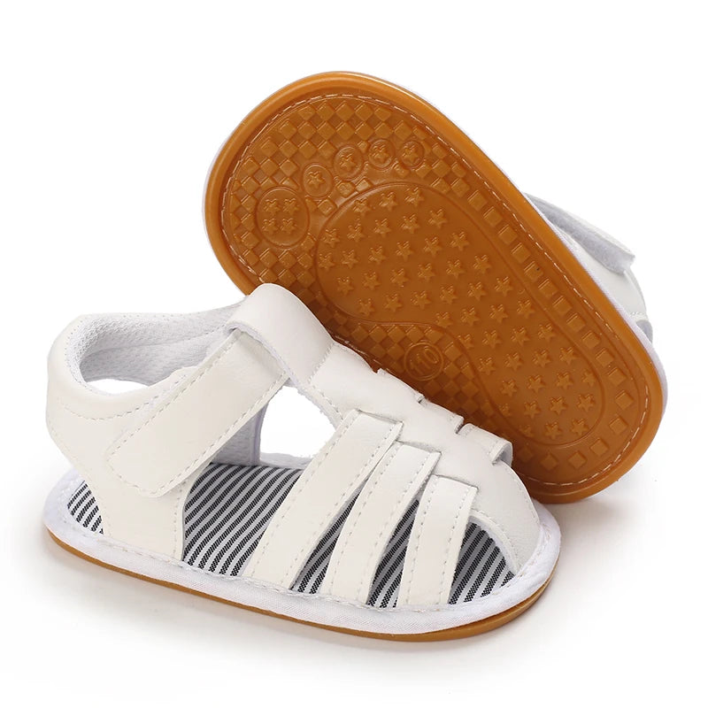 A pair of white baby first walker sandals with a brown anti-slip sole shown next to the shoe.