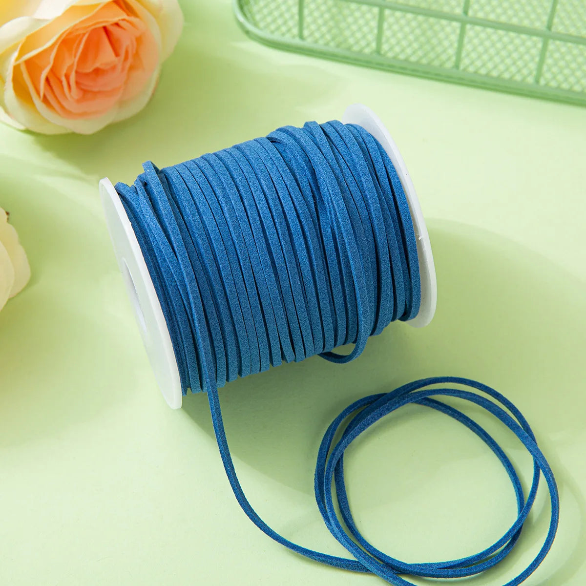 A roll of bright blue velvet faux suede braided ribbon for crafting and gift wrapping lies on a light green surface.
