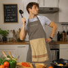 A young man wearing a gray t-shirt and a brown chef apron stands in a kitchen preparing food.