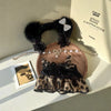 A black lace and leopard print sling dress for plush dolls displayed on a wooden surface.