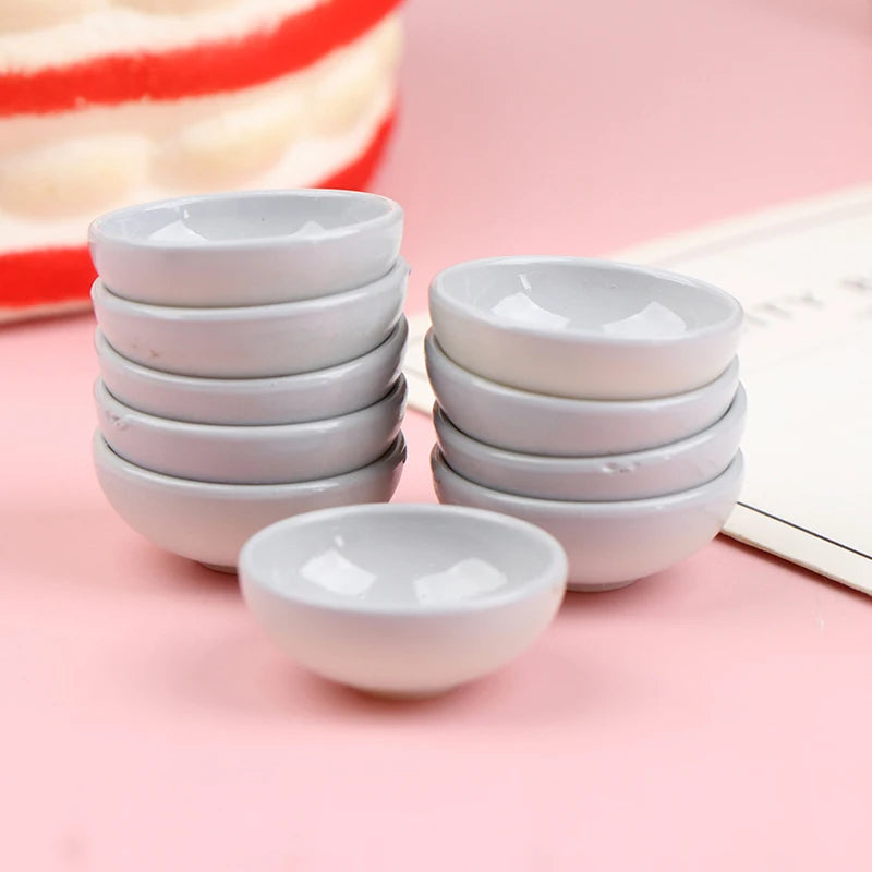 A stack of ten small white ceramic rice bowls is displayed on a pink surface next to a red and white striped object.