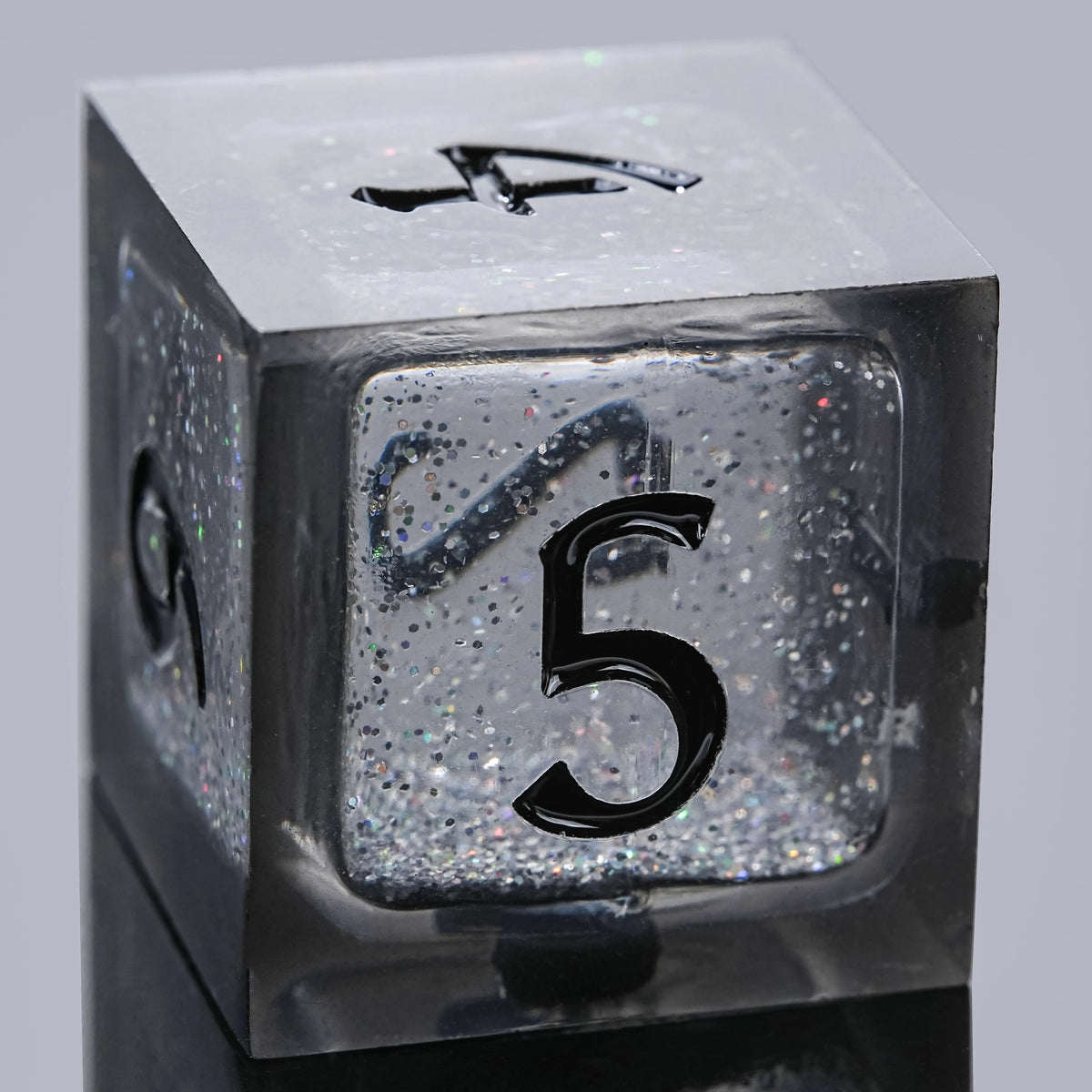 A close-up view of a black liquid core resin dice set featuring a five-sided die with the number 5 visible.