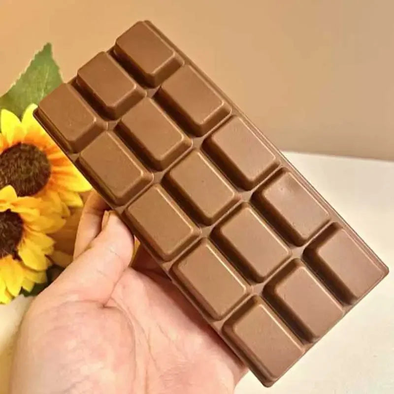 A hand holds a brown, rectangular block of slow rising chocolate sensory squishy fidget toy.