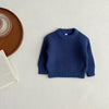A navy blue knit baby pullover sweater lying flat on a light surface next to a wooden plate and a book.