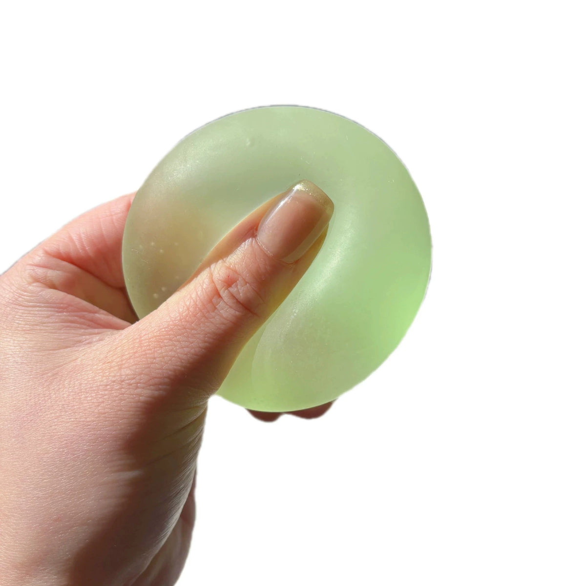A hand holds a translucent light green squishy stress relief toy shaped like a mochi ring.