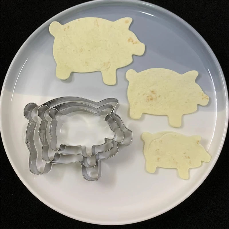 A set of pig-shaped stainless steel cookie cutters on a white plate.