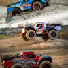 Three RC monster trucks racing across a dirt track in motion