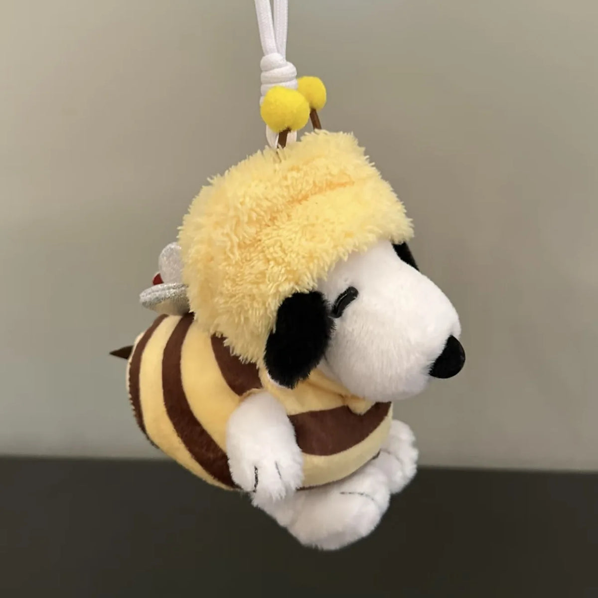A yellow plush Snoopy character with a fluffy yellow hat and black ears, hanging from a white string.