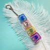 A colorful acrylic fidget keychain featuring four clicky key buttons attached to a silver keyring, resting on white feathers.