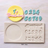 A set of silicone cake molds featuring a yellow circle with the number one and pink text, alongside individual numbers and a 