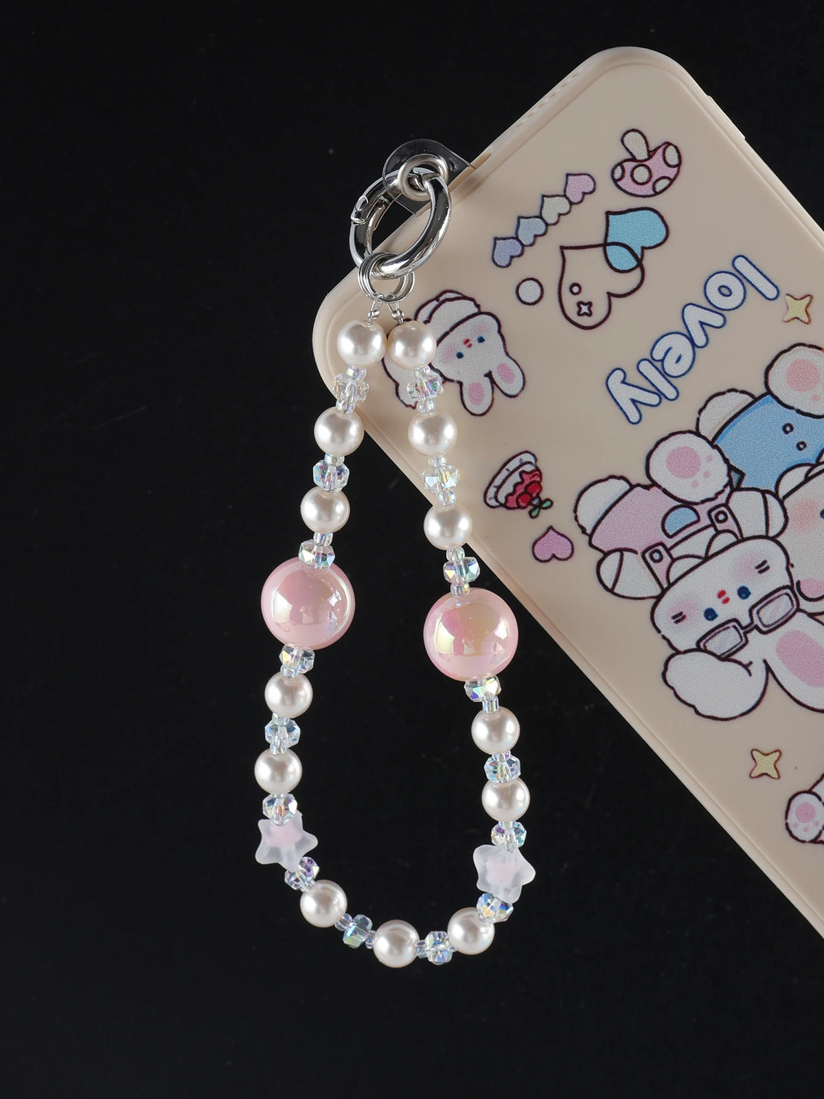 A silver charm featuring pink and clear pearl crystals attached to a bag clip, displayed against a light-colored phone case.