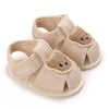 Pair of beige soft sole sandals for baby's first steps featuring bear-themed fabric accents