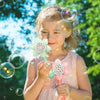 A young girl is blowing bubbles with a sunflower-shaped bubble maker outdoors.