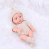A realistic soft vinyl reborn baby doll wearing a knitted outfit and hat, lying on white fluffy fabric.