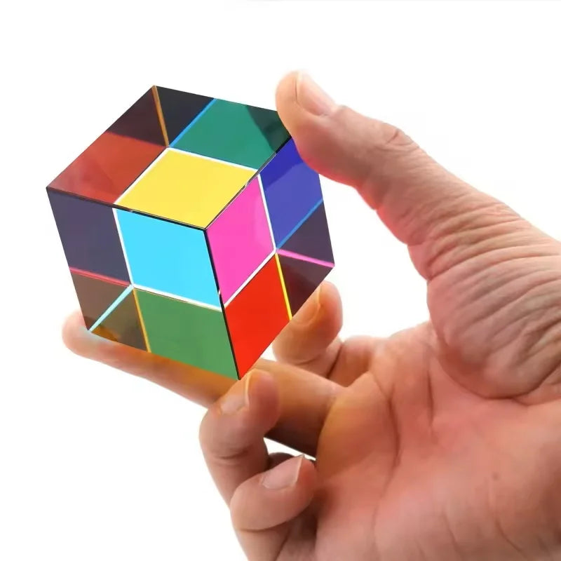 A hand holds a CMY Prism Cube, a 3D color mixing crystal with various colored facets.