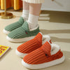 A pair of orange faux fur slippers with white soles and green lining are shown on a light surface.