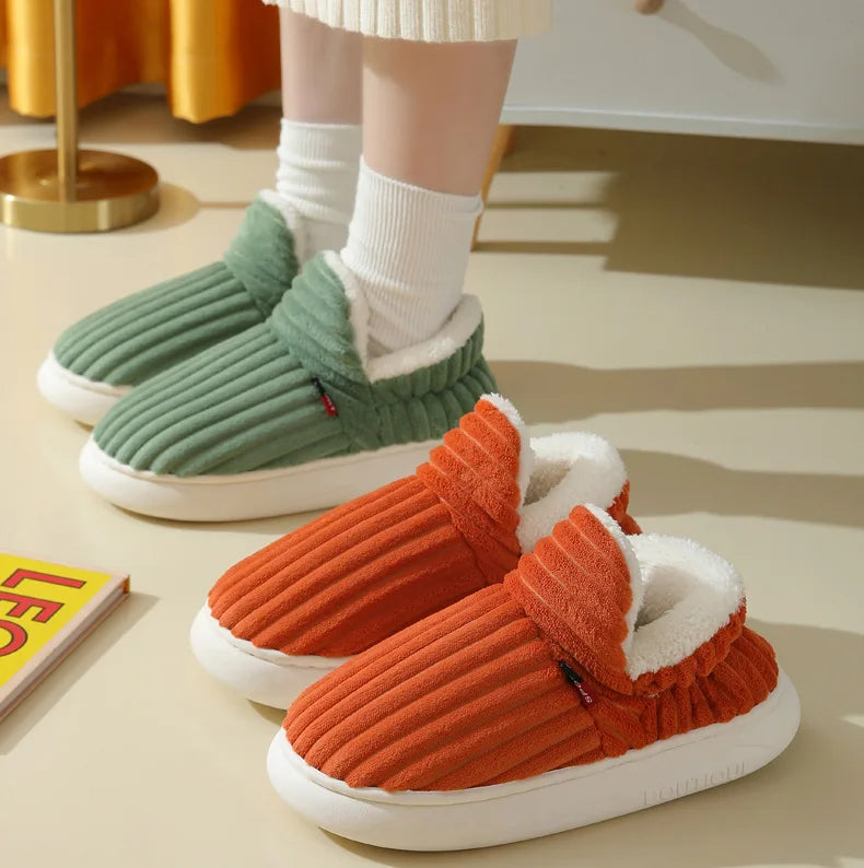 A pair of orange faux fur slippers with white soles and green lining are shown on a light surface.