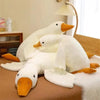 A white goose plush toy with orange beak and feet sitting on a brown surface.