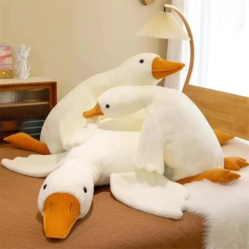 A white goose plush toy with orange beak and feet sitting on a brown surface.