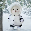 A white plush teddy bear wearing a black and white striped dress standing in the snow.
