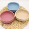 A set of five silicone bowls in pink and beige colors resting on a woven mat.