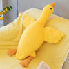 A bright yellow extra-large plush goose pillow with orange feet resting on a yellow textured fabric.