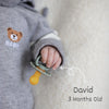 A baby's hand is holding a yellow natural latex pacifier against a soft, light-colored background.